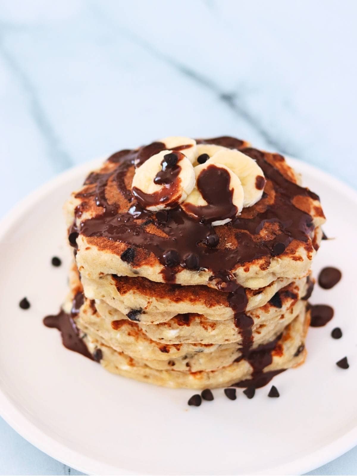 Stack of chocolate chip protein pancakes topped with banana and drizzled with chocolate sauce