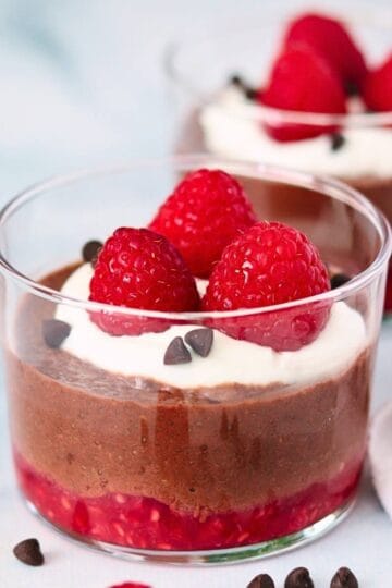 A glass serving of chocolate raspberry chia pudding topped with whipped cream and fresh raspberries.