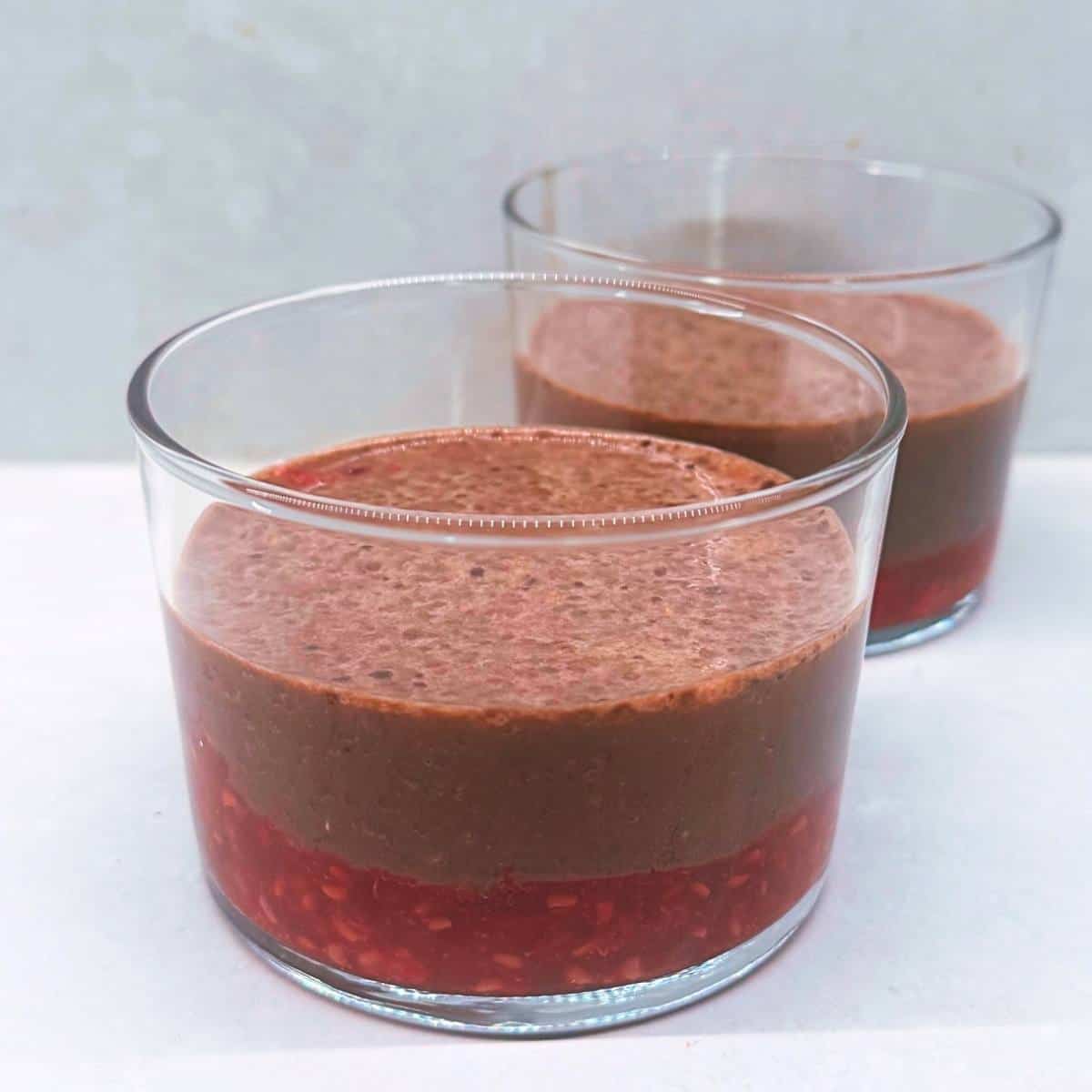 Two glasses of chocolate raspberry chia pudding with chia seeds visible in the layers.