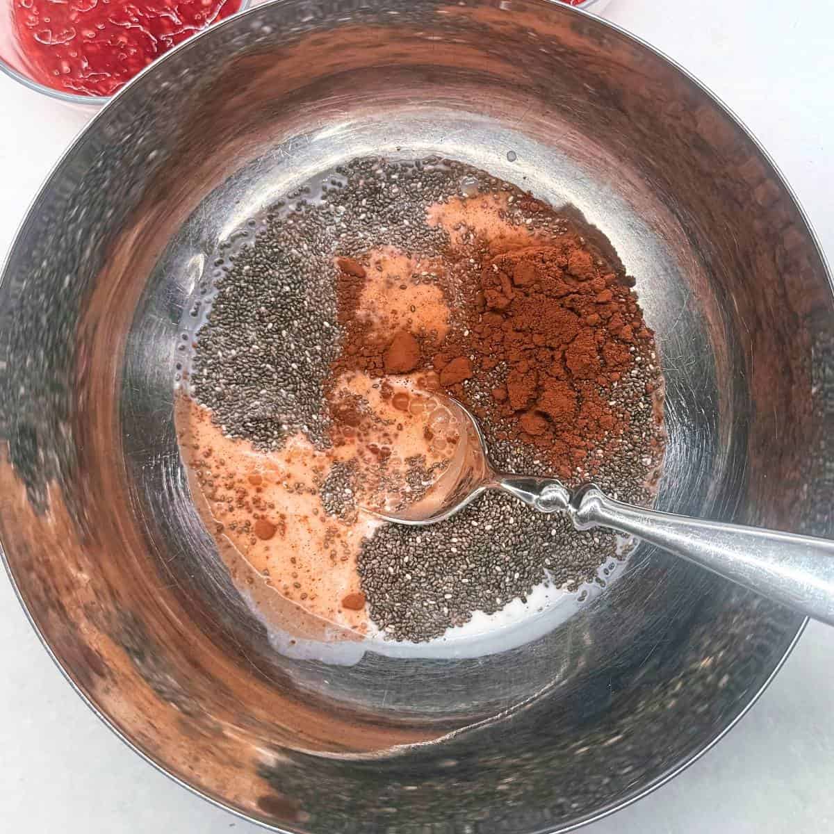 A jar with dark chocolate chia pudding mixture being stirred with a spoon.
