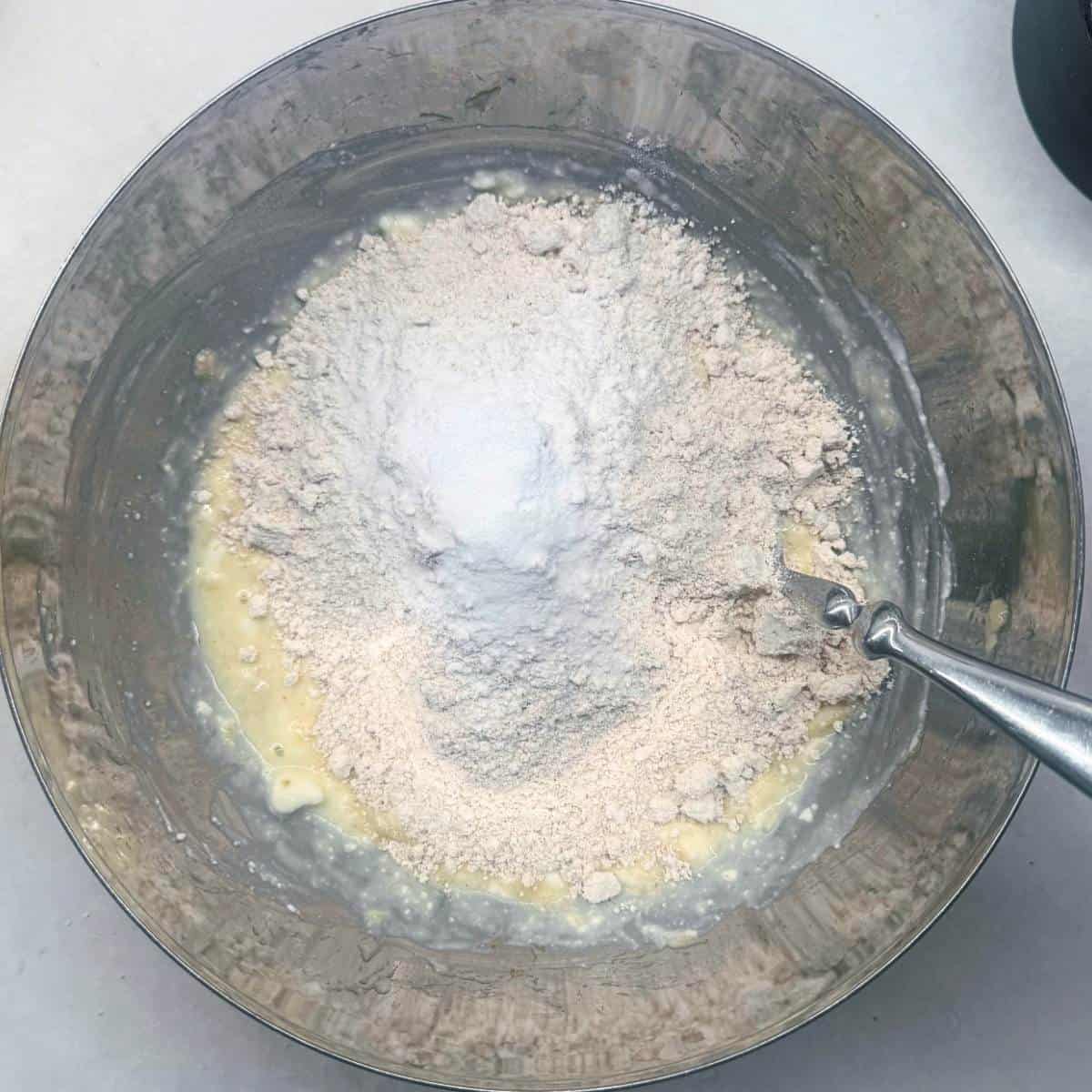 Adding blended oat flour and baking powder to wet ingredients in a mixing bowl