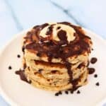 Stack of cooked protein pancakes drizzled with chocolate and topped with chocolate chips
