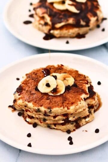 Protein pancakes topped with banana slices and a sprinkle of chocolate chips on a white plate