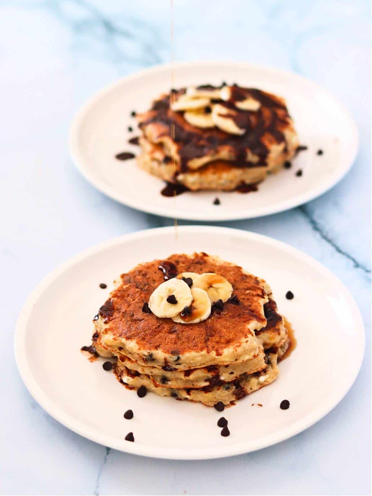 Two plates of protein pancakes topped with banana slices and chocolate chips