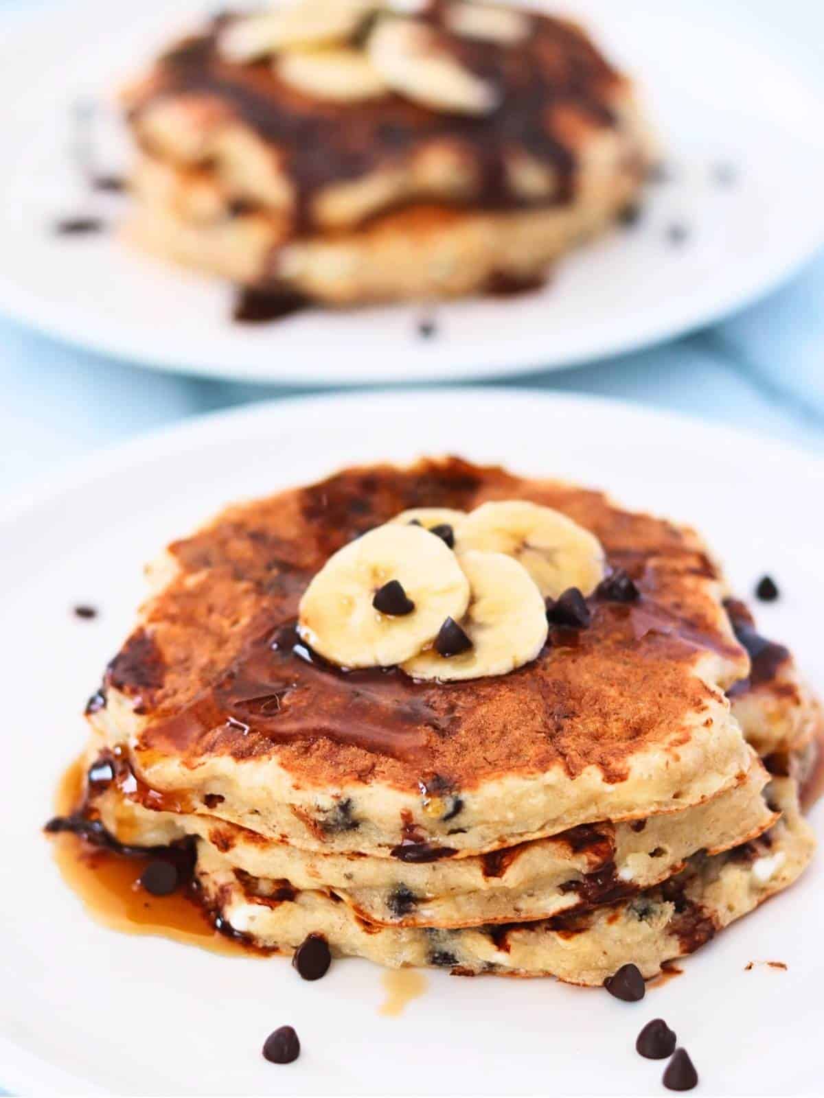 Stack of pancakes with banana slices and chocolate drizzle on a white plate