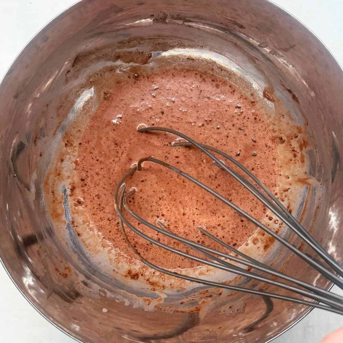 A close-up of the mixture for chocolate chia pudding being whisked in a bowl.